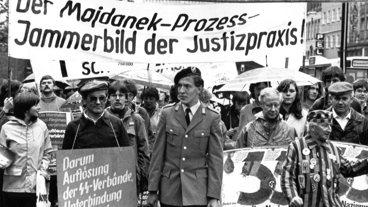 Demonstranten protestieren gegen das Majdanek-Urteil. Ein Mann in Uniform und ein Überlebender des Holocaust tragen Schilder, die gegen NS-Verbrechen und die Verjährung von Taten protestieren.