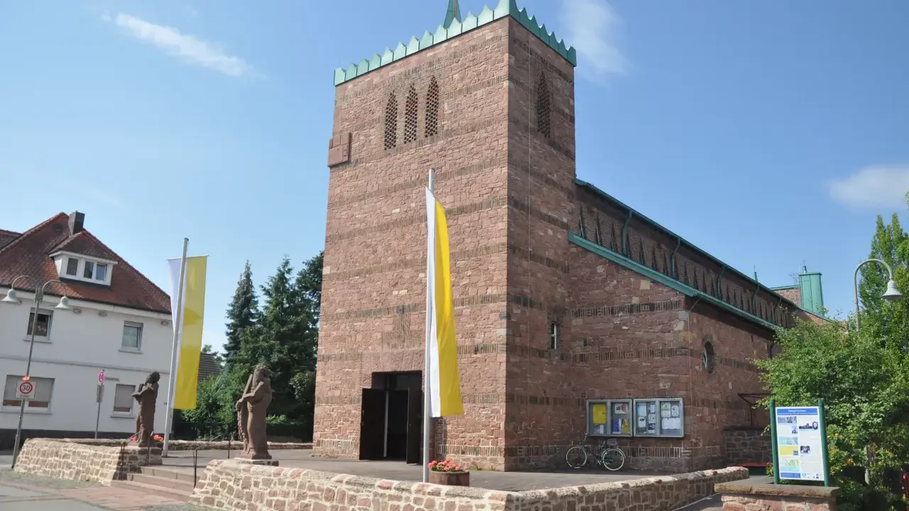 Kirche in Dettingen am Main mit roten Ziegeln, Fahnen und Statuen vor dem Eingang.
