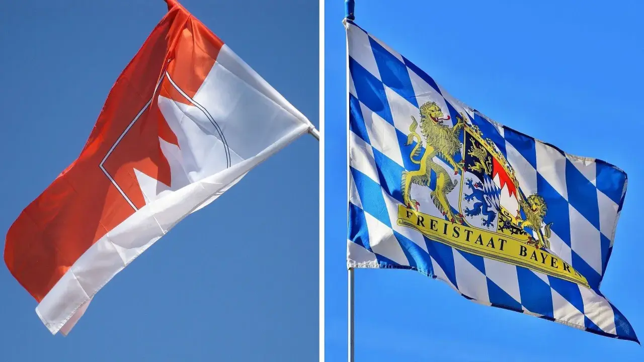 Zwei Fahnen im Wind: eine mit einem roten Ahornblatt, die andere mit dem Wappen des Freistaats Bayern, der stolz seine fränkischen Wurzeln zeigt.