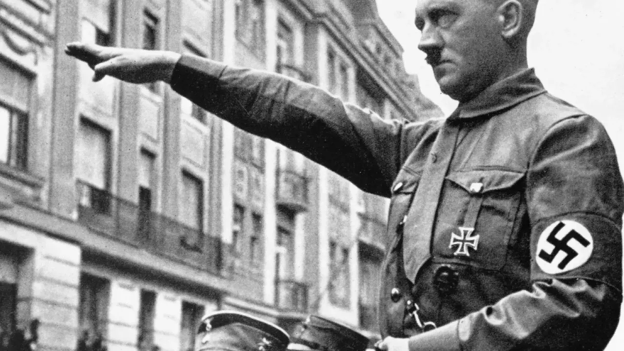 Adolf Hitler hebt den Arm zum Gruß. Seine Uniform zeigt das Hakenkreuz. Die Frage, wie kam Hitler an die Macht, beschäftigt Historiker bis heute.