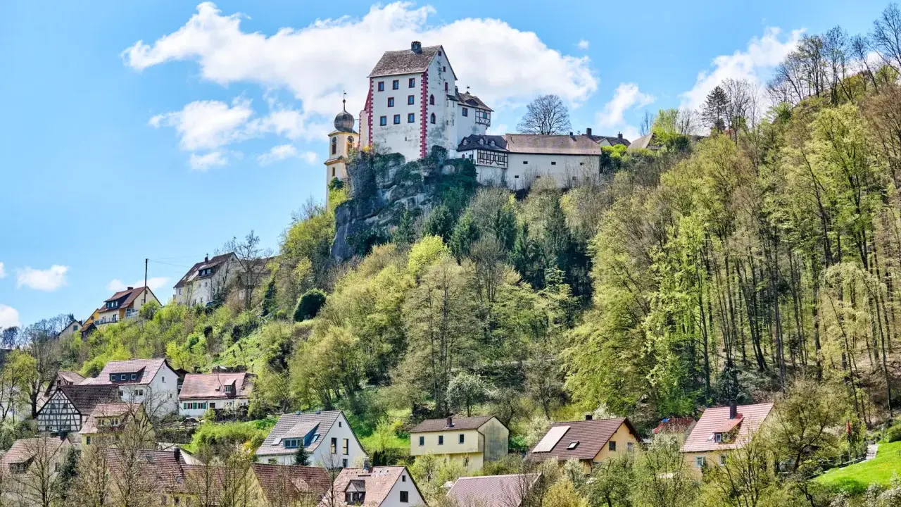 Burg und Dorf von Egloffstein thronen auf einem Felsen unter blauem Himmel mit Wolken.