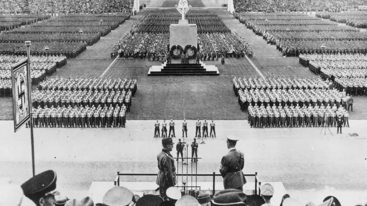 Massenveranstaltung in Nürnberg. Tausende marschieren, Fahnen wehen. Hitler ist anwesend.