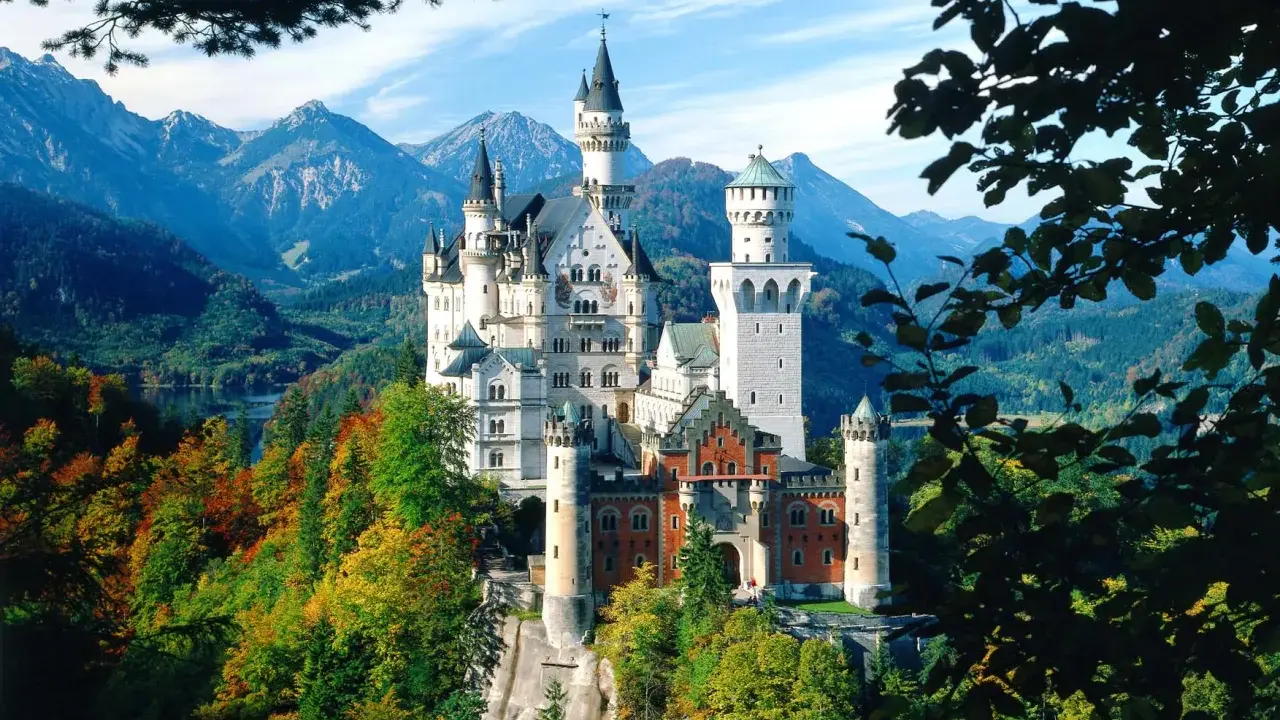 Märchenhaftes Schloss Neuschwanstein thront auf einem Felsen, umgeben von bunten Herbstwäldern und majestätischen Bergen.