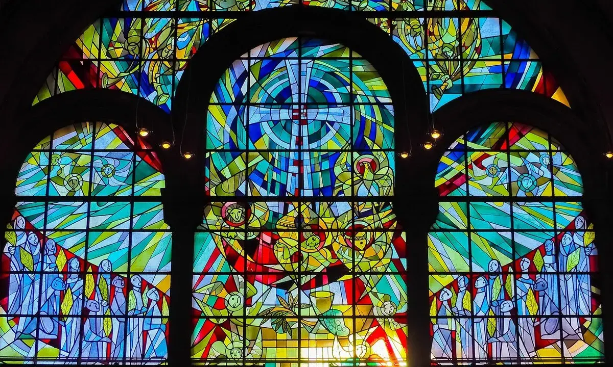 Farbenfrohe Glasmalerei eines Kirchenfensters mit biblischen Szenen und Engeln, die im Licht erstrahlen.