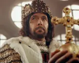 Ein König mit Krone und Hermelinmantel hält ein goldenes Reichsapfel-Kreuz. Er repräsentiert das Lehenswesen und die Macht.