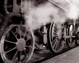 Dampf steigt auf von den Rädern einer historischen Lokomotive, ein Symbol für die Erfindung der Eisenbahn und den Beginn einer neuen Ära.