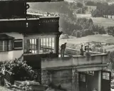 Blick auf die Hitler-Residenz mit Personen auf dem Balkon und einer malerischen Landschaft im Hintergrund.