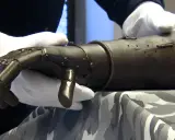 Eine eiserne Prothese, gehalten von Händen in weißen Handschuhen.