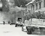 Soldaten der Roten Armee 1945 fahren in einem LKW durch eine verschneite Stadt. Rauch steigt aus einem zerstörten Gebäude auf.