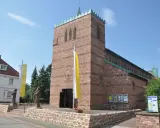 Kirche in Dettingen am Main mit roten Ziegeln, Fahnen und Statuen vor dem Eingang.