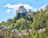 Burg und Dorf von Egloffstein thronen auf einem Felsen unter blauem Himmel mit Wolken.