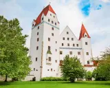 Das weiße Schloss Ingolstadt mit roten Dächern und grünen Bäumen im Vordergrund.
