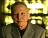 Porträt von Ulrich Enzensberger im Anzug, mit unscharfem, gelb beleuchtetem Hintergrund.