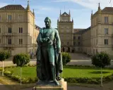 Bronzestatue von Ernst I. vor einem prächtigen Gebäude mit Turm und Arkaden.