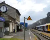 Bahnhof Neunkirchen (Kr Siegen) mit gelb-silbernem Zug auf den Gleisen. Ein Warnschild zeigt einen Zug und eine stürzende Person.
