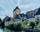 Fachwerkhäuser und ein hoher Turm am Flussufer in Hersbruck, Bayern.