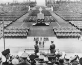 Massenveranstaltung in Nürnberg. Tausende marschieren, Fahnen wehen. Hitler ist anwesend.