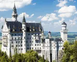 Schloss Neuschwanstein, ein Märchenschloss, dessen Geschichte von König Ludwig II. geprägt ist, thront majestätisch über grünen Hügeln und einem See.