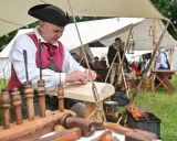 Ein Handwerker in historischer Kleidung arbeitet an Holz. Dies ist ein Beispiel dafür, was ist ein Freilichtmuseum: lebendige Geschichte zum Anfassen.