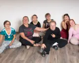 Gruppe von Menschen mit Down-Syndrom und einer Betreuerin sitzen auf dem Boden.