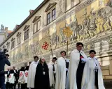 Mitglieder des Ritterordens vom Heiligen Grab zu Jerusalem marschieren vor einem Wandgemälde. Kritik am Orden ist nicht sichtbar.