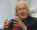Dieter Borchmeyer, mit seinem charakteristischen langen Haar und einem gestreiften Anzug, gestikuliert lebhaft, während er spricht.