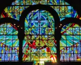 Farbenfrohe Glasmalerei eines Kirchenfensters mit biblischen Szenen und Engeln, die im Licht erstrahlen.