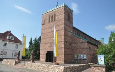 Kirche in Dettingen am Main mit roten Ziegeln, Fahnen und Statuen vor dem Eingang.