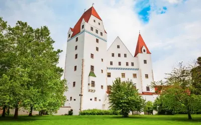 Das weiße Schloss Ingolstadt mit roten Dächern und grünen Bäumen im Vordergrund.