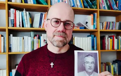 Mann mit Brille hält Foto eines Mannes in Uniform. Im Hintergrund Bücherregale. Das Foto zeigt einen Mann, der der SS Schutzstaffel angehörte.
