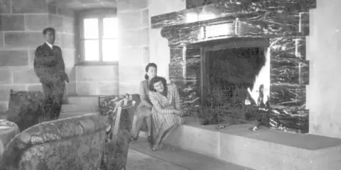 Zwei Frauen entspannen sich 1944 am Kamin im Kehlsteinhaus. Ein Mann steht im Hintergrund.