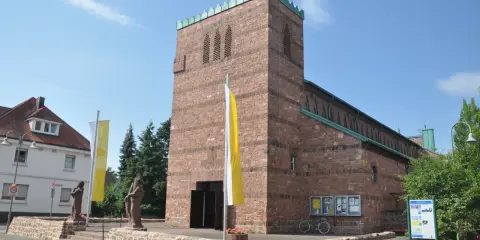 Kirche in Dettingen am Main mit roten Ziegeln, Fahnen und Statuen vor dem Eingang.