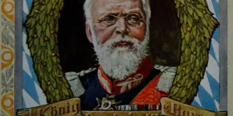 König Ludwig III. von Bayern, mit weißem Bart und Brille, umrahmt von einem Lorbeerkranz.