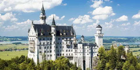 Schloss Neuschwanstein, ein Märchenschloss, dessen Geschichte von König Ludwig II. geprägt ist, thront majestätisch über grünen Hügeln und einem See.