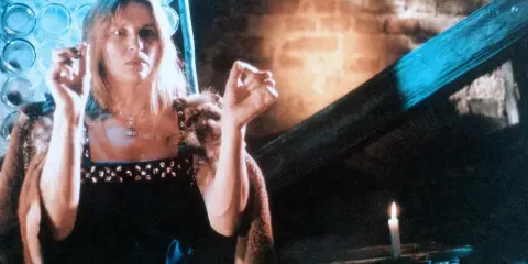 Annamirl Bierbichler in dunklem Kleid mit Pelzmantel, die Hände erhoben, im Schein einer Kerze.