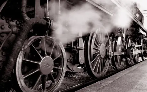 Dampf steigt auf von den Rädern einer historischen Lokomotive, ein Symbol für die Erfindung der Eisenbahn und den Beginn einer neuen Ära.