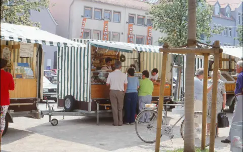 Marktstände in Neukirchen Balbini mit Brot und Butter. Menschen kaufen ein, ein Fahrrad steht bereit.