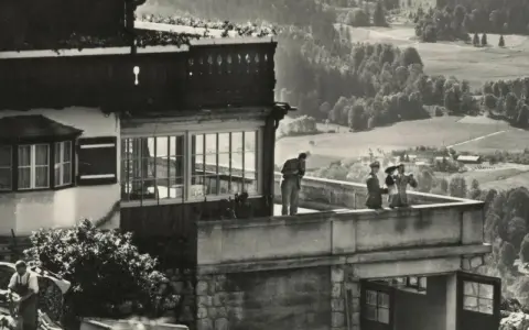Blick auf die Hitler-Residenz mit Personen auf dem Balkon und einer malerischen Landschaft im Hintergrund.