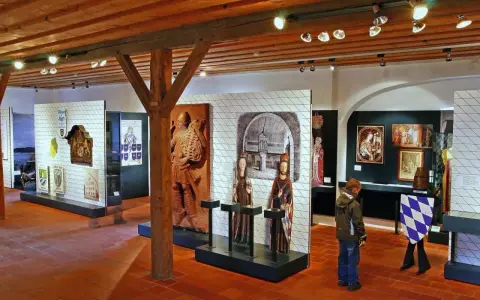 Museumsausstellung mit historischen Artefakten, darunter das Wittelsbacher Wappen, Skulpturen und Gemälde.