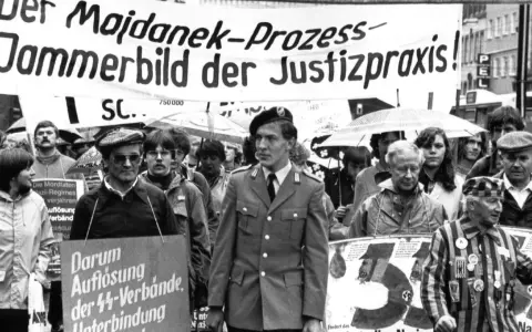 Demonstranten protestieren gegen das Majdanek-Urteil. Ein Mann in Uniform und ein Überlebender des Holocaust tragen Schilder, die gegen NS-Verbrechen und die Verjährung von Taten protestieren.