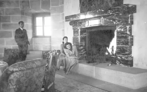 Zwei Frauen entspannen sich 1944 am Kamin im Kehlsteinhaus. Ein Mann steht im Hintergrund.