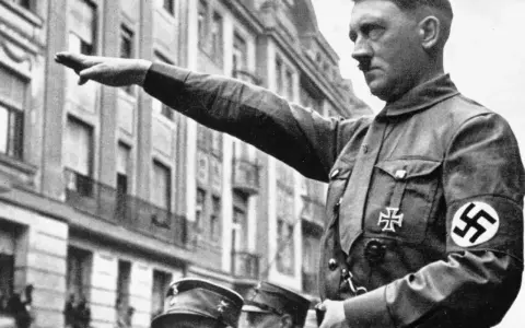 Adolf Hitler hebt den Arm zum Gruß. Seine Uniform zeigt das Hakenkreuz. Die Frage, wie kam Hitler an die Macht, beschäftigt Historiker bis heute.