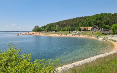 Sonniger Strandtag am Rothsee bei Heideck, Bayern. Menschen entspannen sich am Sandstrand, während Segelboote auf dem Wasser gleiten.