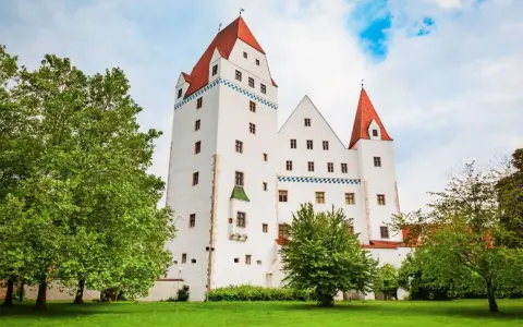 Das weiße Schloss Ingolstadt mit roten Dächern und grünen Bäumen im Vordergrund.