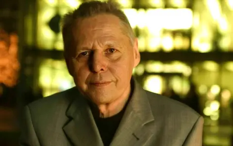 Porträt von Ulrich Enzensberger im Anzug, mit unscharfem, gelb beleuchtetem Hintergrund.