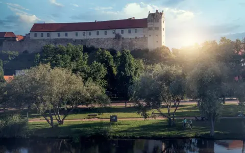 Schloss hinter Bäumen, ein Fluss im Vordergrund. Ein friedlicher Tag, wie ihn die Wettiner heute genießen könnten.