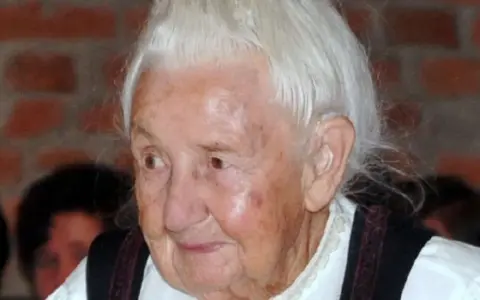 Porträt einer älteren Frau mit weißem Haar und traditioneller Kleidung. Traudl Well lächelt sanft.