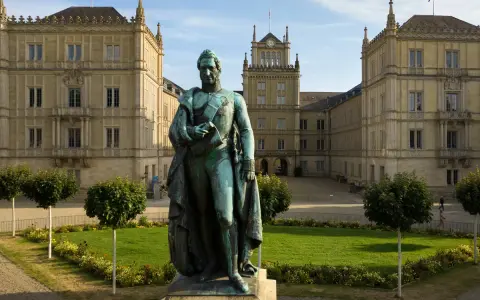 Bronzestatue von Ernst I. vor einem prächtigen Gebäude mit Turm und Arkaden.