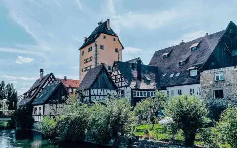 Fachwerkhäuser und ein hoher Turm am Flussufer in Hersbruck, Bayern.