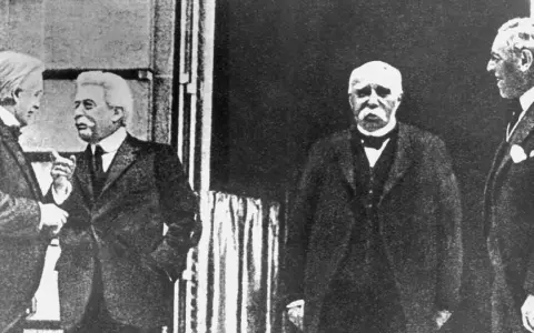 Vier Männer in Anzügen, die über den Friedensvertrag von Versailles diskutieren.